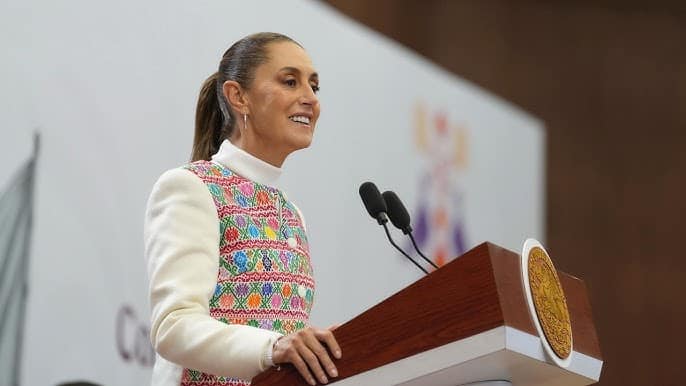 Mujer sonriente dando un discurso en un podio durante un evento oficial en un entorno formal.