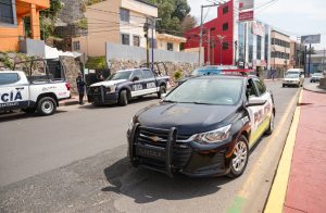 Vehículos de policía en una calle de Tlaxcala, México, con varias unidades estacionadas y un edificio moderno al fondo, durante el día.
