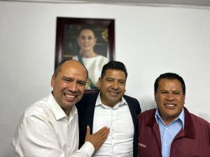 Hombres sonriendo en una reunión formal, con un retrato de una mujer en la pared detrás de ellos.