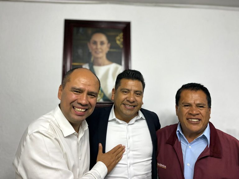 Hombres sonriendo en una reunión formal, con un retrato de una mujer en la pared detrás de ellos.