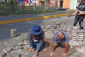 Personas reparando y colocando adoquines en una calle, trabajando en un proyecto de pavimentación en Tlaxcala, México, durante el día.