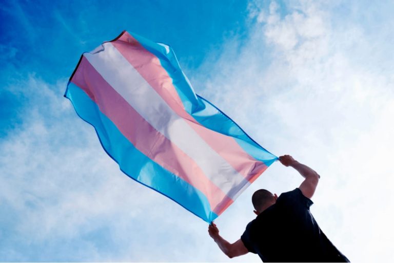 Transgénero bandera transgénero ondeada por una persona contra el cielo azul con nubes.