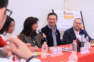 Panel de discusión con varios participantes en una mesa, en un evento de Tlaxcala, con logotipos y materiales relacionados con el evento BAMX.