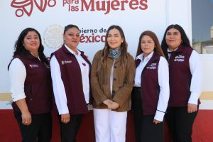 Mujer con vestimenta formal y chaqueta marrón, sonriendo, en un evento organizado por el gobierno de México para promover los derechos de las mujeres.