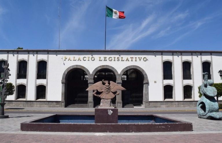 Edificio del Palacio Legislativo de Tlaxcala con bandera mexicana ondeando en el techo y esculturas en el patio central, en un día soleado y despejado.
