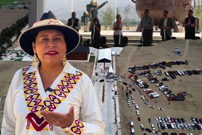 Mujer indígena tlaxcalteca con vestimenta tradicional y sombrero, en un evento público con modelos de autos y personas observando en el fondo.