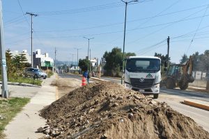 Un camión y maquinaria de construcción trabajan en una calle de Tlaxcala, México, con una pila de tierra y señalización vial, en medio de un proyecto de mejora urbana en un día soleado.