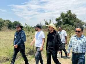 Grupo de personas caminando en campo abierto con árboles y cielo despejado, en un día soleado.