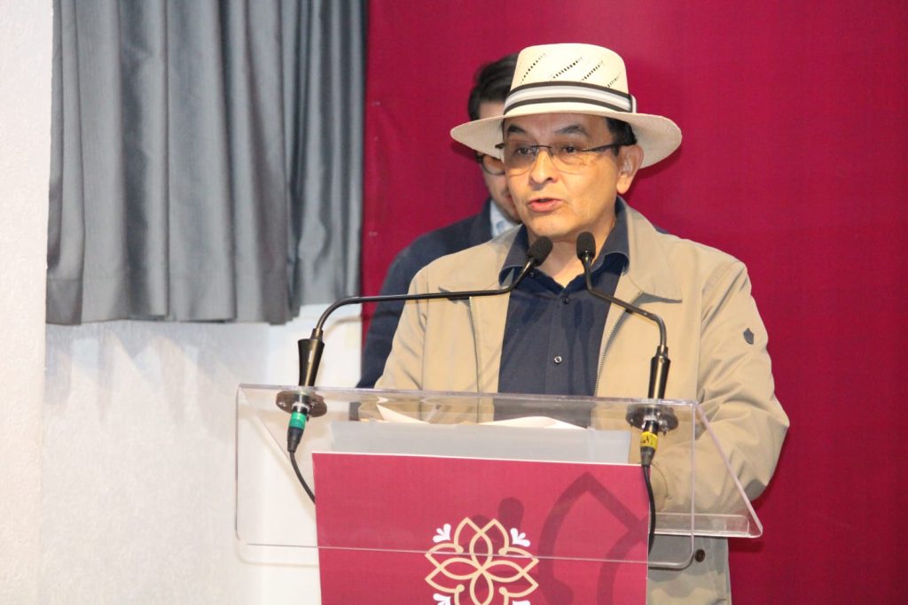 Hombre con sombrero y gafas hablando en un podio durante un evento en Tlaxcala, México.