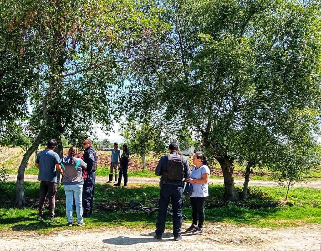 Grupo de personas reunidas en un parque con árboles y senderos, conversando y caminando en un entorno natural.