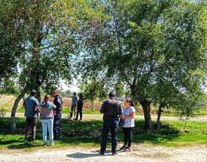 Grupo de personas reunidas en un parque con árboles y senderos, conversando y caminando en un entorno natural.