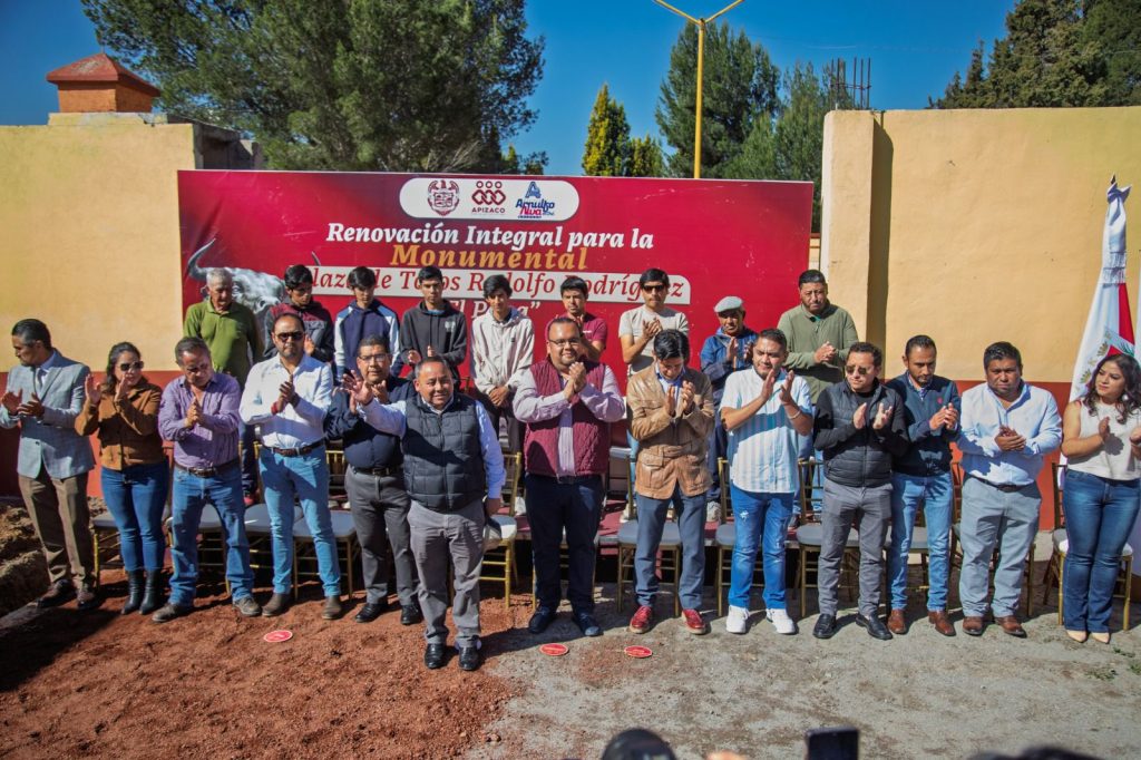 Grupo de personas en ceremonia de inauguración de la restauración del monumento en Tlaxcala, con fondo de cartel y árboles, en un día soleado y despejado.