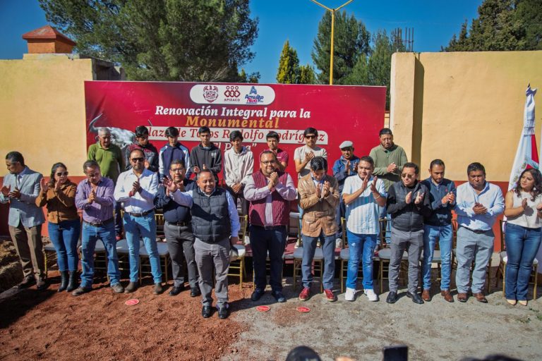 Grupo de personas en ceremonia de inauguración de la restauración del monumento en Tlaxcala, con fondo de cartel y árboles, en un día soleado y despejado.