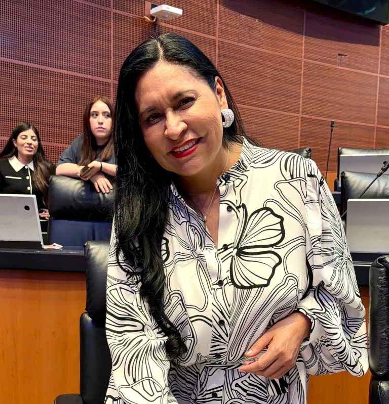 Mujer sonriente en una reunión formal, con fondo de sala de conferencias y otras personas en el evento.