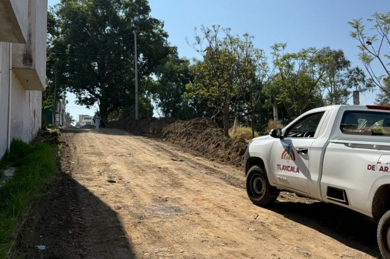 La camioneta de la autoridad de Tlaxcala estacionada en una calle de tierra en un área rural, con árboles y un cielo despejado en el fondo.