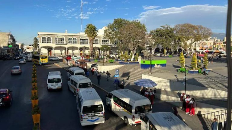 Plaza principal de Tlaxcala con vehículos y personas en un día soleado, rodeada de árboles y edificios históricos.