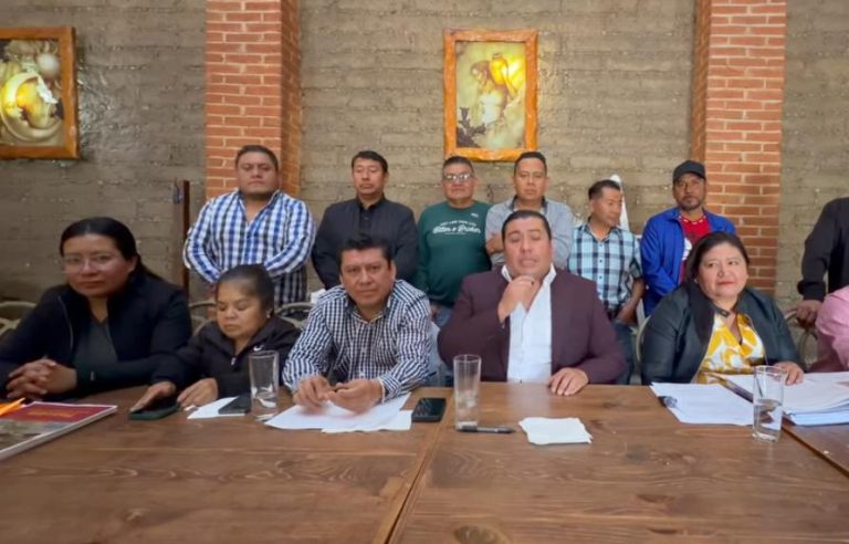 Grupo de personas en una reunión formal en un espacio con paredes de ladrillo y cuadros decorativos, en Tlaxcala, México.