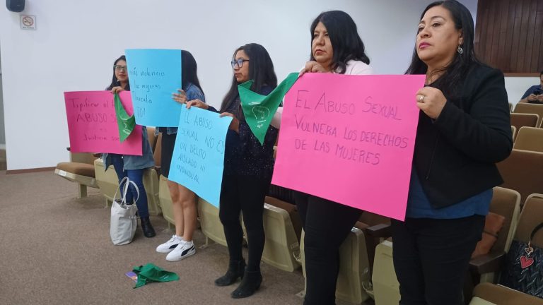 Protesta contra el abuso sexual y la vulneración de derechos de las mujeres en Tlaxcala, con mujeres sosteniendo carteles en una manifestación pacífica en un auditorio.