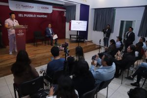 Presentador en evento de Tlaxcala durante una conferencia con audiencia y medios de comunicación presentes.