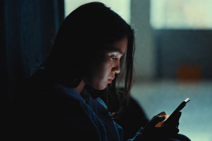 Una joven mujer usando un teléfono móvil en un ambiente oscuro y tranquilo.