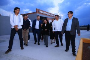 Grupo de personas caminando frente a la entrada de la Universidad Nacional Autónoma de México, en un día nublado.