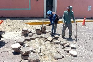 Reparación de pavimento en calle de Tlaxcala con trabajadores colocando adoquines en una vía pública.