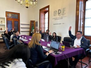 La reunión de un grupo de personas en una sala de conferencias, con algunos levantando la mano, en un entorno formal y profesional.