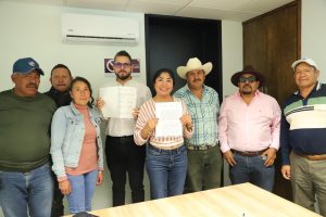 Grupo de personas en una reunión, algunos con documentos en mano, en un ambiente de oficina, celebrando un acuerdo o logro importante.