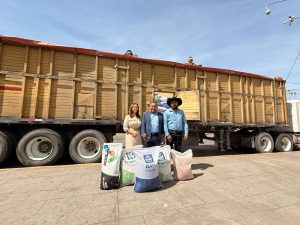 Cargando un tren de madera en una plataforma, con tres personas de pie frente a las bolsas de productos, en un día soleado en Tlaxcala, México.
