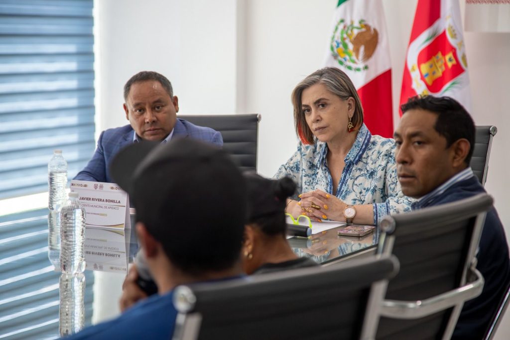 Reunión oficial con funcionarios en una sala de conferencias, con banderas de México y Tlaxcala al fondo.