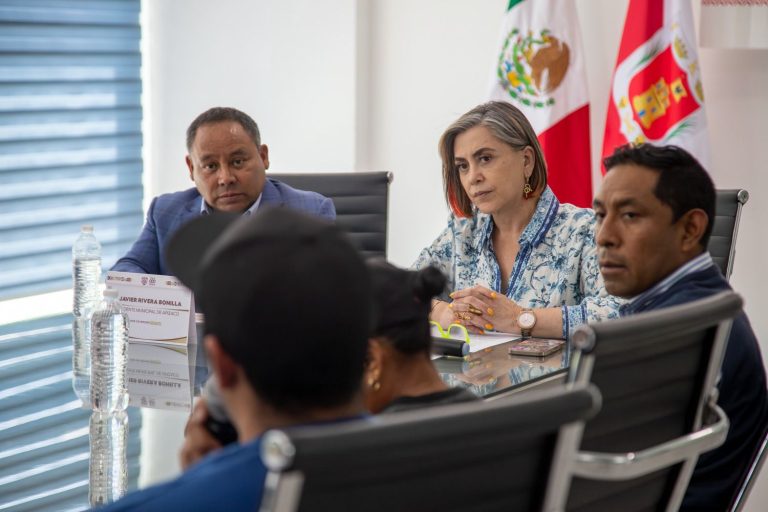 Reunión oficial con funcionarios en una sala de conferencias, con banderas de México y Tlaxcala al fondo.