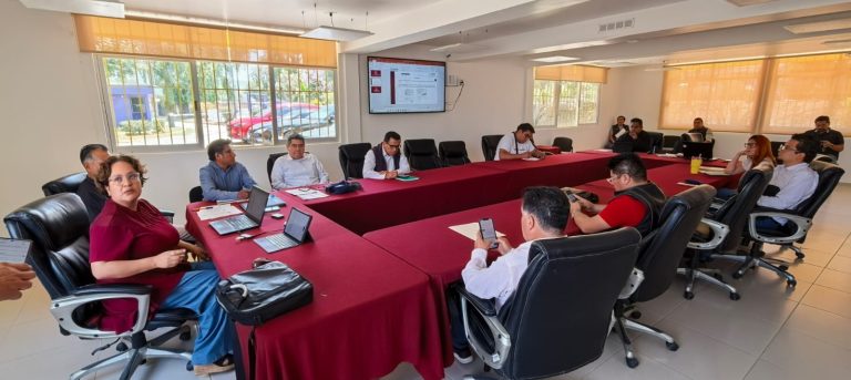 Reunión de profesionales en una sala de conferencias moderna con pantallas digitales y laptops, participando en una discusión o presentación importante.