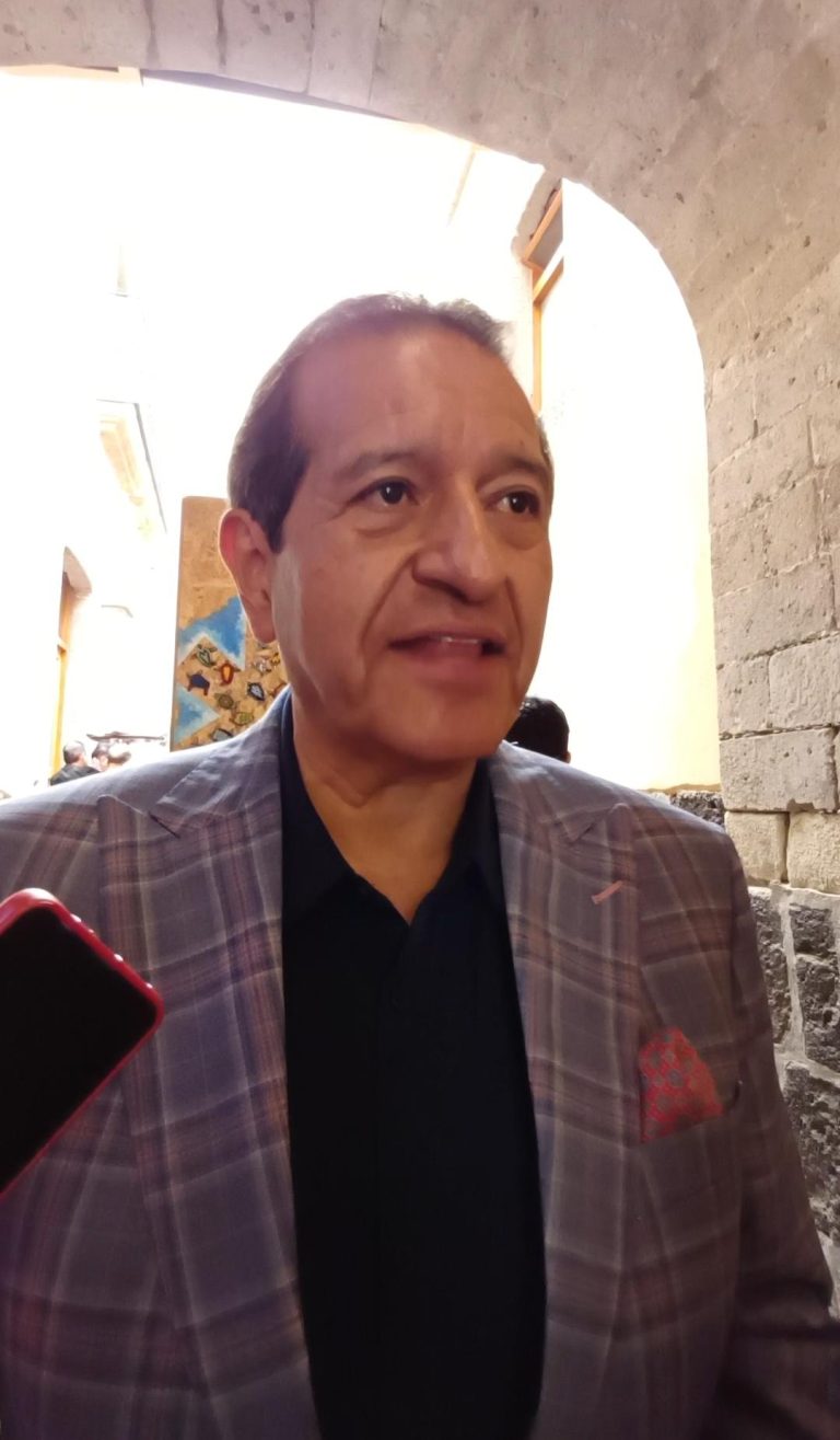 Hombre en un entorno histórico con arcos y paredes de piedra, vestido con traje a cuadros y camisa negra, en una entrevista o evento público en Tlaxcala, México.