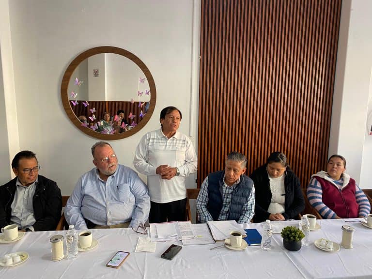 Grupo de personas en una reunión formal en una sala moderna, participando en una discusión o presentación.