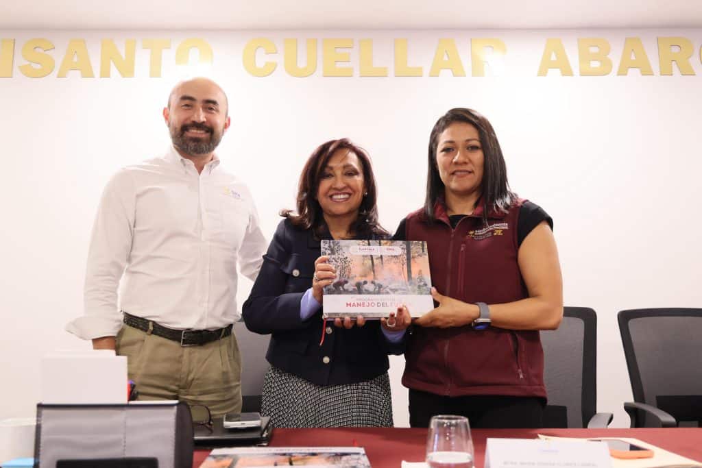 Persona entregando un reconocimiento en una reunión formal, con fondo que dice "SANTO CUELLAR ABAR".