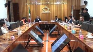 La reunión del Instituto Tlaxcalteca de Elecciones en una sala con participantes y pantallas digitales en la mesa.