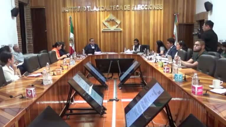 La reunión del Instituto Tlaxcalteca de Elecciones en una sala con participantes y pantallas digitales en la mesa.