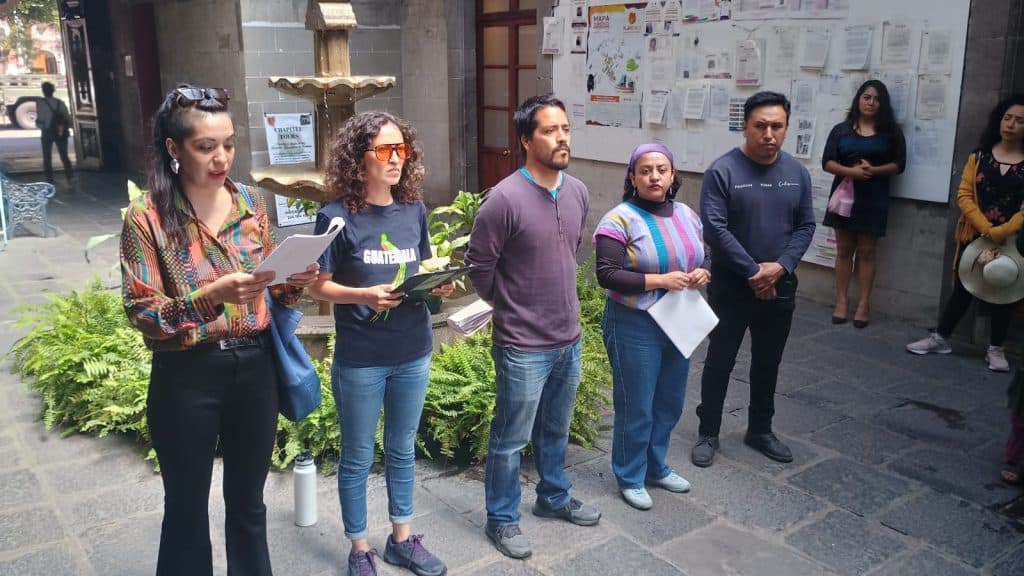 Persona leyendo un documento durante una manifestación en la calle en Tlaxcala, México, con varias personas observando en el fondo.