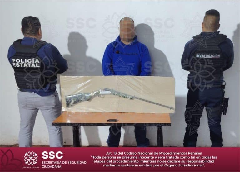 Persona detenido entre dos policías estatales, con un arma asegurada sobre una mesa, en una escena de investigación policial en Tlaxcala, México.