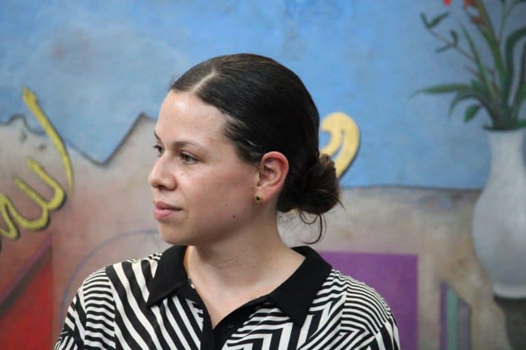 Mujer con cabello recogido y blusa a rayas en un entorno artístico con mural colorido de fondo.