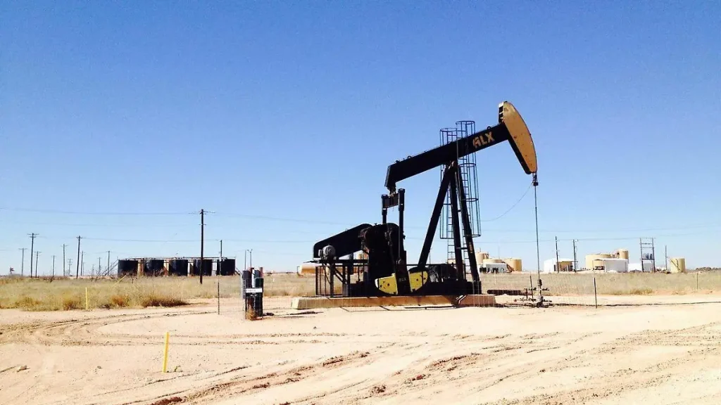 Técnico de extracción de petróleo en un campo petrolero en un paisaje árido con cielo despejado.
