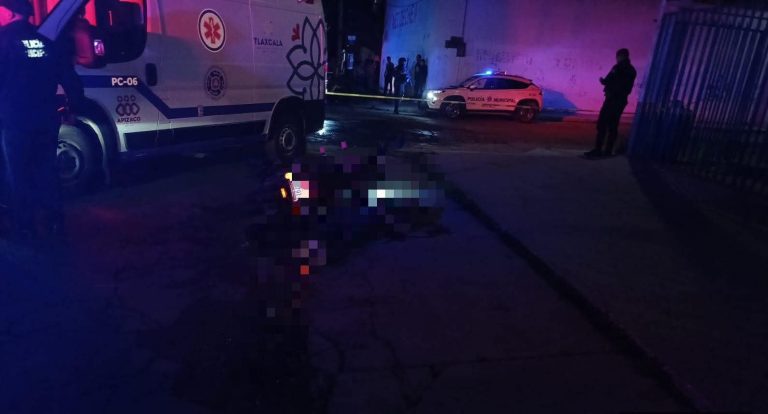 Escena de un accidente nocturno con una ambulancia y una patrulla en Tlaxcala, México, con presencia policial y un vehículo accidentado en la calle.