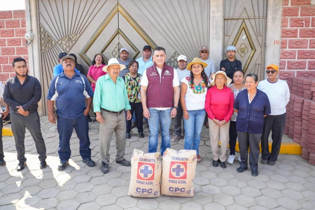 Grupo de personas con bolsas de cemento y equipo de protección en una calle de Tlaxcala, participando en una actividad comunitaria o de ayuda social.