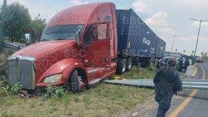 Accidente de tráiler en la autopista, vehículo volcado y daños en la vía, con presencia de personal de emergencia y policías en la escena.
