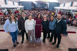 Grupo de siete personas en un evento público con gran asistencia en un espacio abierto y moderno, durante el día.