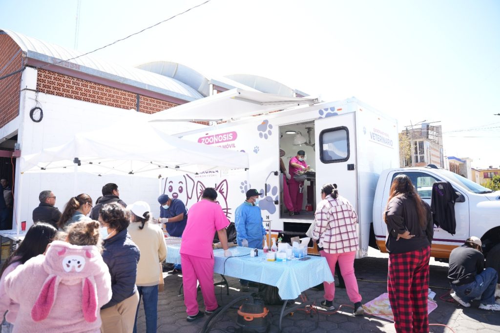 Unidad móvil de salud atendiendo a la comunidad en una calle de Tlaxcala, con personal médico y personas esperando servicios médicos en un evento al aire libre.