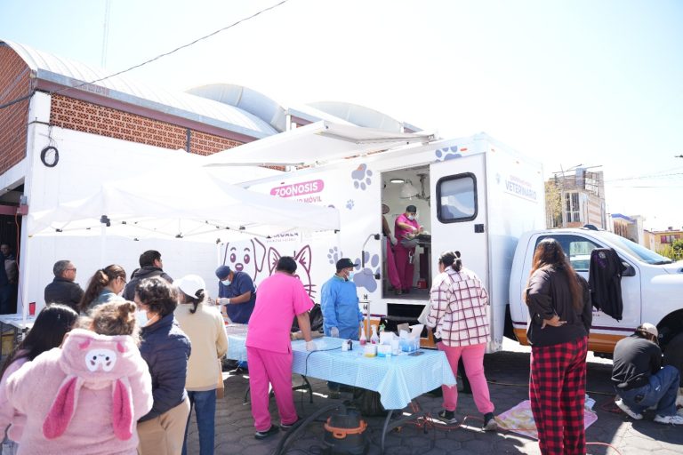 Unidad móvil de salud atendiendo a la comunidad en una calle de Tlaxcala, con personal médico y personas esperando servicios médicos en un evento al aire libre.