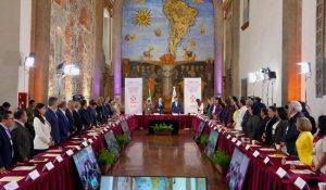 Reunión oficial en un salón con mural del mundo y participantes de pie en una ceremonia formal.