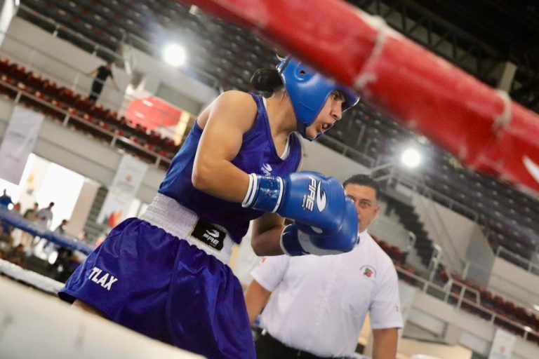 Boxeadora femenina en el ring durante una competencia, con equipo de protección azul y concentrada en la pelea.