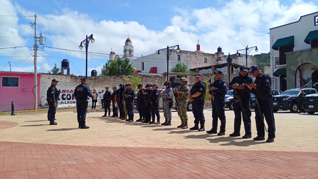 Policías en formación en una plaza pública de Tlaxcala, México, durante un ejercicio de entrenamiento o simulacro, con edificios y cielo nublado de fondo.